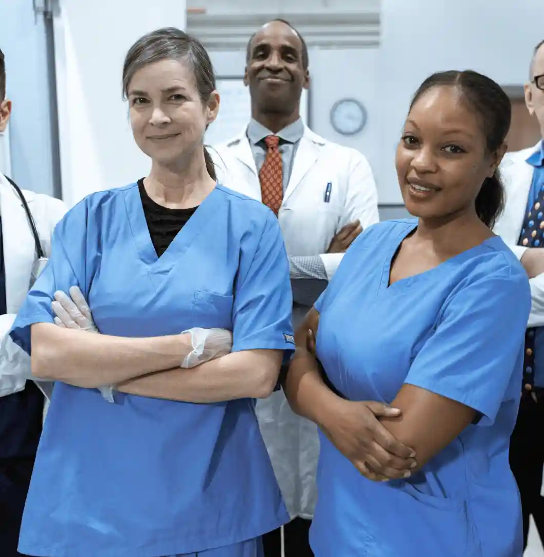A diverse group of four medical professionals, including two women and two men, all wearing blue scrubs, standing together with their arms crossed in a medical setting.