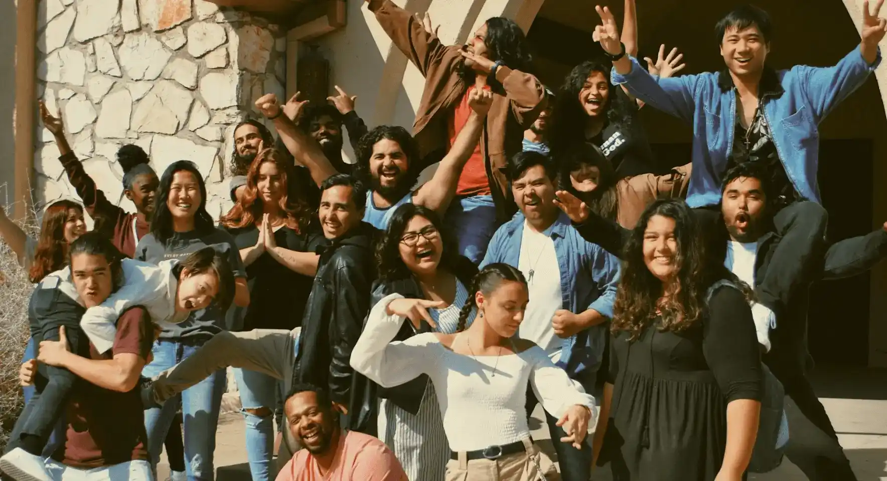A group of young people posing and having fun outdoors, with some giving peace signs and playful expressions.