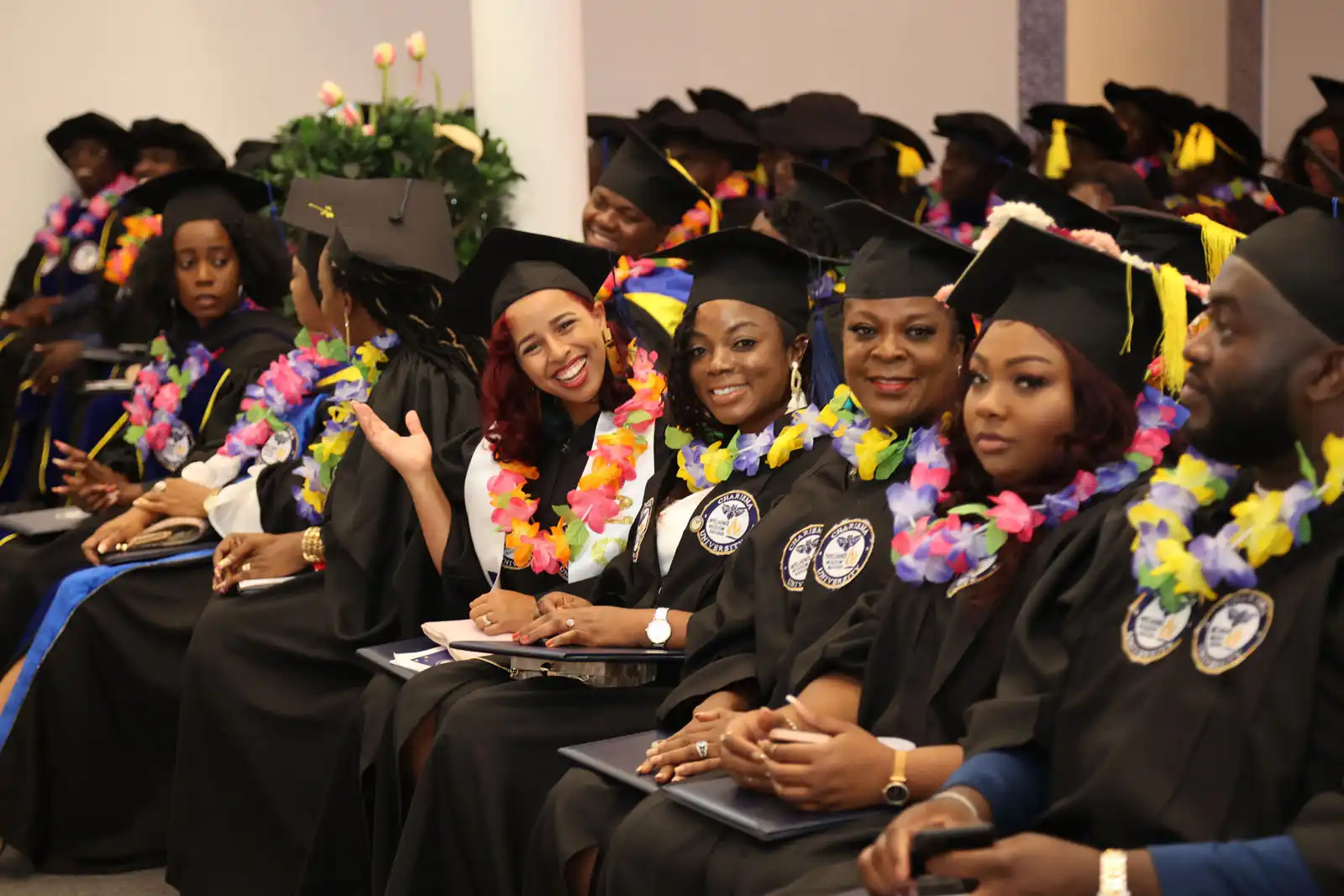 A group of graduates in caps and gowns, wearing colorful leis, smiling and posing at a graduation ceremony.