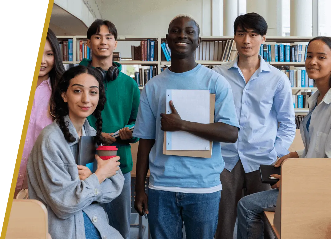 A diverse group of six students smiling and posing together in a library setting.